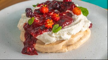 Sobre um prato cinza de pedra, está a pavlova com um coullis de pitanga, pitangas inteiras e ramos de hortelã enfeitando a geleia vermelha que está por cima do chantilly de coco e da pavlova. Foto: Tomás Rangel